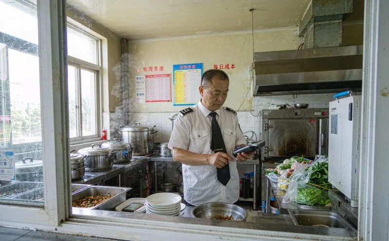 中国食堂管理员在打餐窗口前用手持终端统计当餐订餐人数并与菜品成本表核对