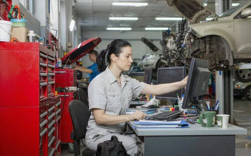 中国汽车维修门店的车间里,一名技师正俯身检修车辆底盘,背景是整齐的工具架与举升机