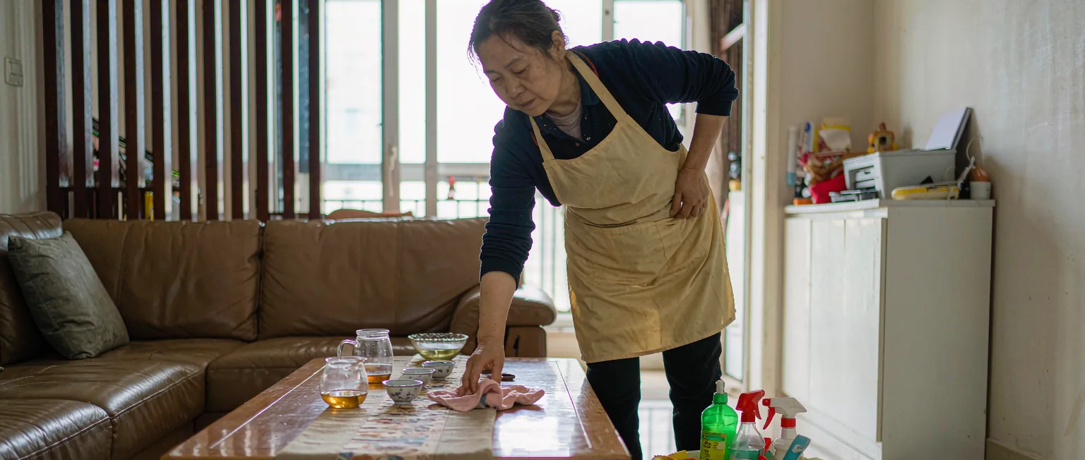 一位中国家政服务人员手持手机在客户家门口扫码打卡上户,背景是居民小区楼道