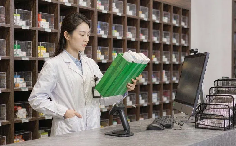 中国连锁药店的门店里,执业药师正在货架前为顾客拿取药品,背景是整齐的药品陈列与价签